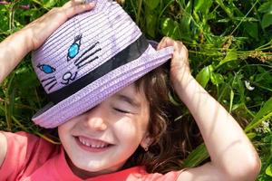 Portrait of a child in a hat with his face covered in summer lying in the grass and wildflowers. Hat with eyes and ears like a cat, summer time, freedom photo