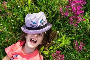 retrato de un niño en un sombrero con su cara cubierto en verano acostado en el césped y flores silvestres sombrero con ojos y orejas me gusta un gato, verano tiempo, libertad foto