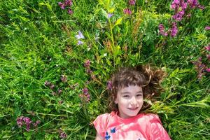 Portrait of a child girl in summer lying in the grass and wildflowers with heels and palms. summer time, freedom photo