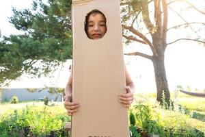 The child is funny dancing and fooling around in a box costume - round cutout for face and hands. Moving to a new house, children's games from improvised means, a suit with your own hands photo