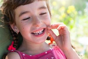 sin dientes contento sonrisa de un niña con un caído inferior Leche diente de cerca. cambiando dientes a molares en infancia foto