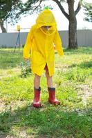 A girl in red rubber boots and a yellow raincoat runs through puddles after a rain in the village. Summer time, freedom, childhood photo