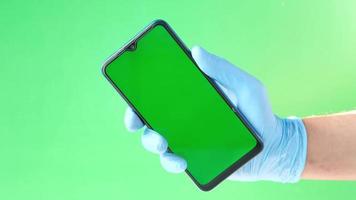 Hand in latex gloves holding smart phone against green background video