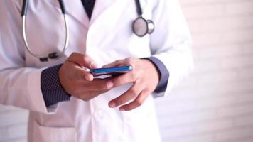 mano del medico che tiene in mano uno smartphone con schermo vuoto sulla scrivania della clinica video