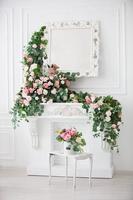 Vertically, the interior of a white room decorated with pink flowers. White fireplace, mirror and flower garlands. photo