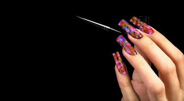 Hand with a beautiful manicure and a brush on a black background. Nail design. Extended nails. photo