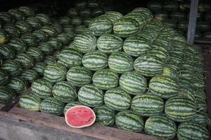 The neatly arranged pile of watermelons with one fruit cut open revealing its red flesh. These watermelons are being sold at a fruit market in Thailand photo