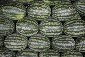 The neatly arranged pile of watermelons with one fruit cut open revealing its red flesh. These watermelons are being sold at a fruit market in Thailand photo