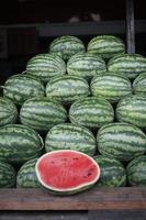 The neatly arranged pile of watermelons with one fruit cut open revealing its red flesh. These watermelons are being sold at a fruit market in Thailand photo