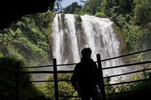 Silhouette man on the cave in front of great water fall, Semarang Central Java. The photo is suitable to use for adventure content media, nature poster and forest background.