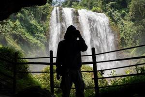 Silhouette man on the cave in front of great water fall, Semarang Central Java. The photo is suitable to use for adventure content media, nature poster and forest background.