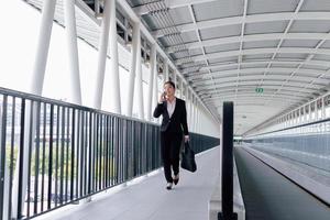 joven asiático mujer de negocios en negro traje utilizando digital tableta y en pie en pasarela estación con Copiar espacio. foto