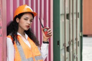 retrato de hembra trabajador en carga contenedores en Envío envase patio trasero. mujer participación walkie-talkie y digital tableta. foto