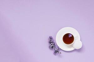 Flower arrangements of beautiful purple lilac on a purple background with a cup of tea. Women's office desk, stylish stock image, Flat layout, top view with Empty copy space photo