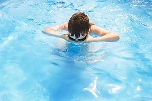 boy dives in swimming pool with swimming glasses. boy swims in the pool. child learning to swim photo