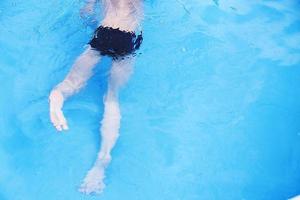 chico nada en el piscina. chico aprendizaje a nadar. pies en el piscina cerca foto