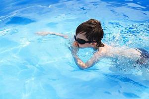 boy dives in swimming pool with swimming glasses. boy swims in the pool. child learning to swim photo