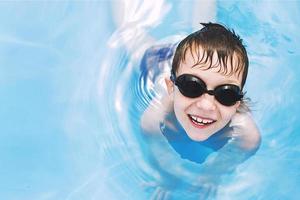 contento bebé en el piscina. chico nada en el piscina con nadando lentes. . chico aprendizaje a nadar foto