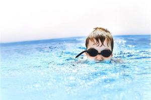 boy dives in swimming pool with swimming glasses. boy swims in the pool. child learning to swim photo