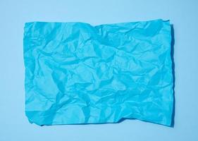 Crumpled rectangular sheet of blue paper on a blue background, top view. Place for inscription photo