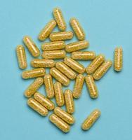 Transparent medical capsules with yellow granules inside on a blue background, tablets for treatment, vitamins photo