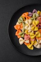 Raw farfalle pasta in different colors on a dark concrete background photo