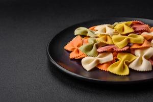 Raw farfalle pasta in different colors on a dark concrete background photo