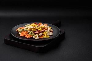 Raw farfalle pasta in different colors on a dark concrete background photo