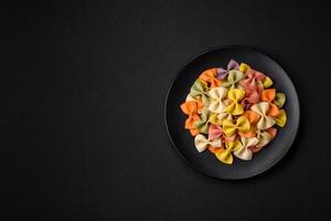 Raw farfalle pasta in different colors on a dark concrete background photo