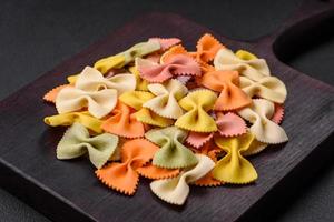 Raw farfalle pasta in different colors on a dark concrete background photo