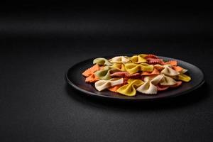 Raw farfalle pasta in different colors on a dark concrete background photo