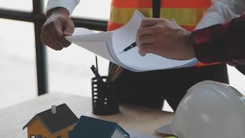 costruzione e struttura concetto di ingegnere o architetto incontro per progetto Lavorando con compagno e ingegneria utensili su modello edificio e planimetria nel Lavorando luogo, contrarre per tutti e due aziende. video