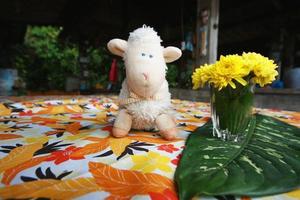 Happy sheep doll with yellow flowers and beautiful fern leave decoration on colorful Tablecloth and table in coffee shop photo