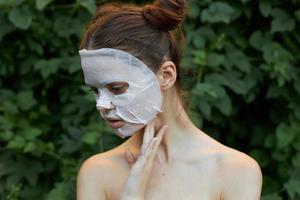 Portrait of a girl face mask Looks down and holds his hand near his neck bare shoulders bushes in the background photo