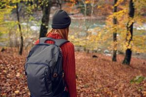 woman in a sweater with a backpack on her back near the river in the mountains and park trees autumn landscape photo