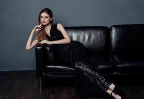 Elegant woman in a dark dress on a leather sofa and evening makeup photo