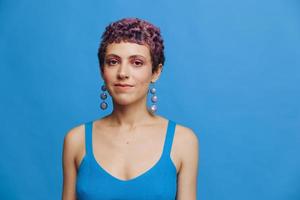 joven atlético Moda mujer con de colores pelo y corto Corte de pelo posando y bailando en azul ropa de deporte sonriente y mirando a el cámara de cerca en un azul monocromo antecedentes foto