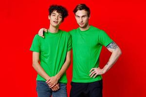 two men in green t-shirts are standing side by side communication isolated background photo