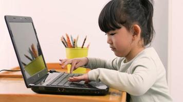 pequeño niña utilizando ordenador portátil jugando juegos en línea a hogar. niño y artilugio concepto. mi aprendiendo, moderno tecnología concepto. lado ver video
