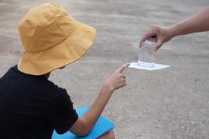 Student boy wears hat, hold book, learning science experiment about air pressure from glass of water which covered by paper. Concept, science subject activity, education. Learning by doing. Observe. photo