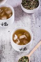 Iced green japanese hojicha tea in cups and leaves in a bowl on the table vertical view photo