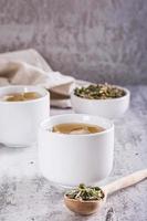 Cold green Japanese hojicha tea with ice in cups and dry tea in a bowl on the table. Vertical view photo