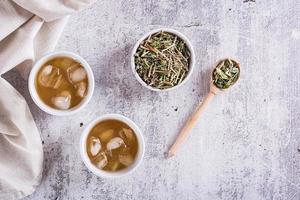 Cold green Japanese hojicha tea with ice in cups and dry tea in a bowl on the table. Top view photo