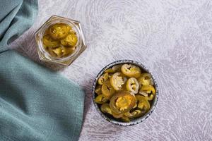 Sliced pickled jalapeno peppers in bowl and glass jar on table top view photo