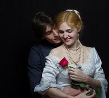 hermosa Pareja en retro estilo. un hombre abrazos un mujer. niña en un blanco vestir con un rojo Rosa en un antecedentes de un hombre. foto