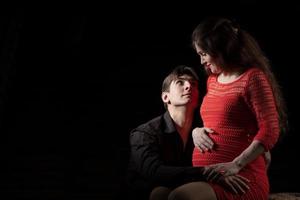 hermoso hombre abrazos un hermosa embarazada esposa en un oscuro antecedentes. foto