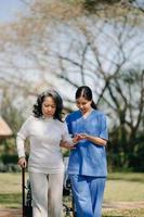 Elderly asian senior woman on wheelchair with Asian careful caregiver. Nursing home hospital garden concept. photo