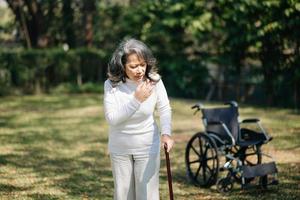 Asian old woman sitting on a wheelchair outdoors in the park Have pain in the arms, wrists and body in sun light photo