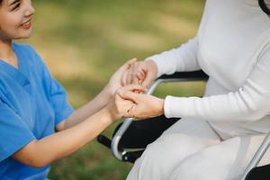 Elderly asian senior woman on wheelchair with Asian careful caregiver. Nursing home hospital garden concept. in sun light photo