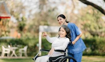 mayor asiático mayor mujer en silla de ruedas con asiático Cuidado cuidador y animar paciente, caminando en jardín. con cuidado desde un cuidador y mayor salud seguro. foto